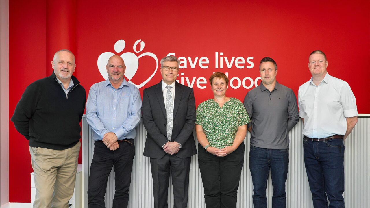 The project delivery team stood together in front of a red wall