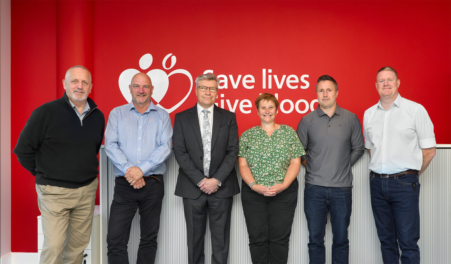 The project delivery team stood together in front of a red wall