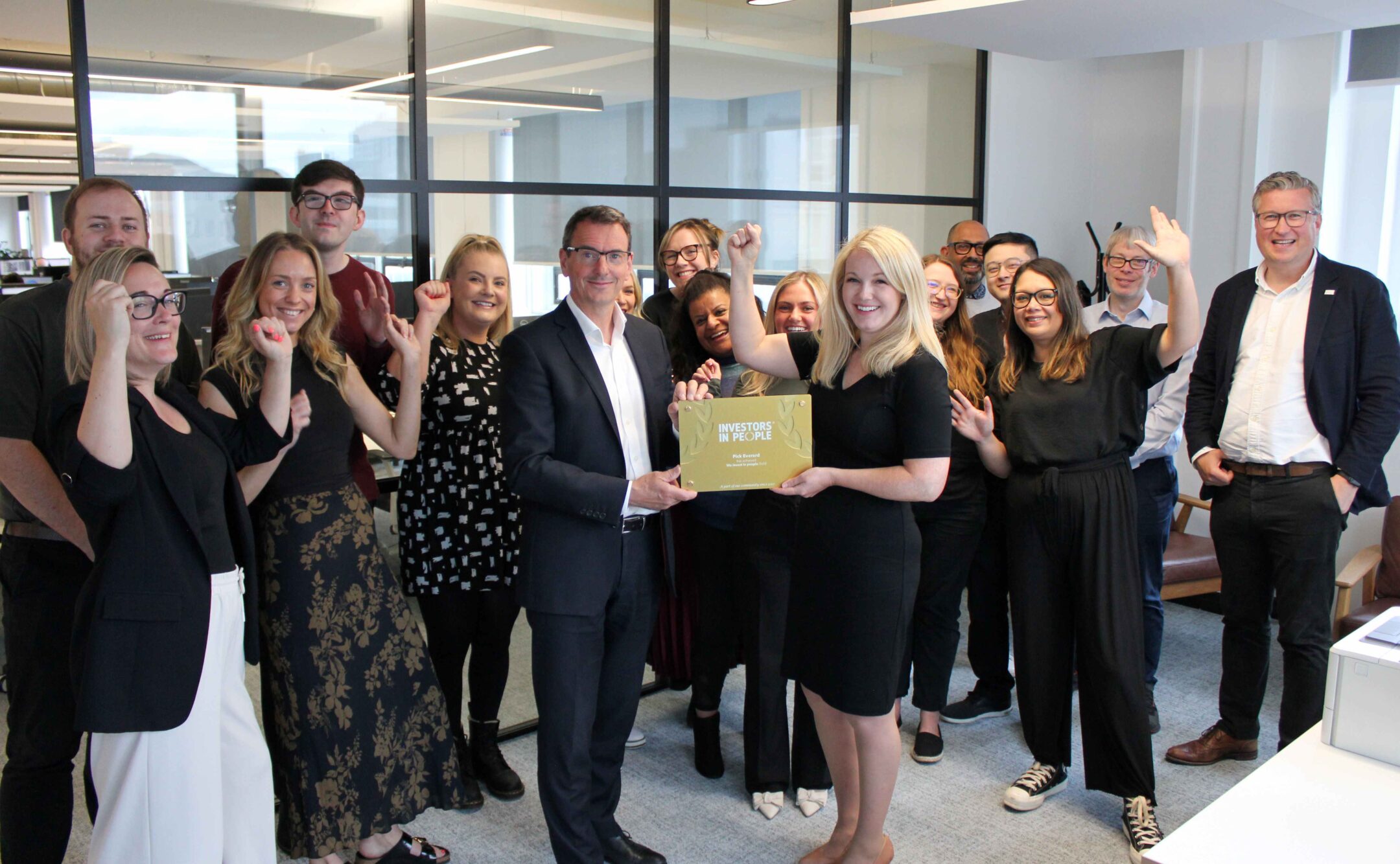 A cheerful group of people poses for a picture, holding a the investors in people gold plaque.